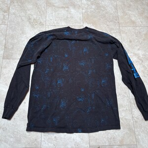 May include: Black long-sleeve shirt with a blue pattern and blue text on the left sleeve. The shirt is made of a soft material and is suitable for casual wear.