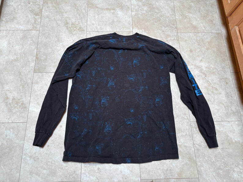 May include: Black long-sleeve shirt with a blue pattern and blue text on the left sleeve. The shirt is made of a soft material and is suitable for casual wear.
