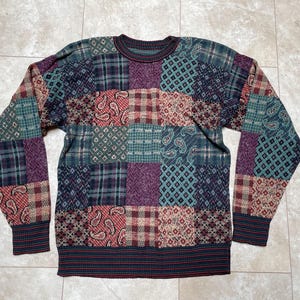 May include: A multi-colored patchwork sweater with a crew neck. The sweater is made of a soft, knitted fabric and features a variety of different patterns, including paisley, plaid, and geometric designs.