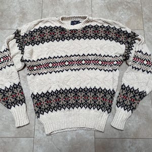 Może przedstawiać: Wełniany sweter w kolorze kremowym z geometrycznym wzorem w kolorze czarnym, czerwonym i brązowym.