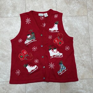 May include: Red knitted vest with a button-up front and embroidered winter holiday designs. The designs include ice skates, mittens, and snowflakes.