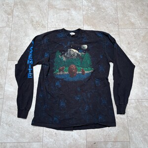 May include: Black long-sleeve shirt with a nature scene featuring bears, trees, and a mountain. The sleeve has the word "YOSEMITE" in blue. The shirt has a dark blue and black pattern.