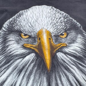 May include: Close-up graphic of an eagle's head. The eagle features white and grey feathers, a yellow beak, and intense yellow eyes. The background is a dark grey colour.