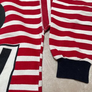 May include: Red and white striped long-sleeve shirt with a black and white graphic of Mickey Mouse. The shirt has a navy blue cuff.