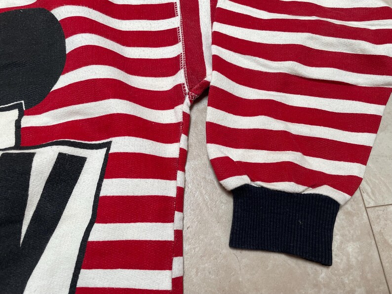 May include: Red and white striped long-sleeve shirt with a black and white graphic of Mickey Mouse. The shirt has a navy blue cuff.