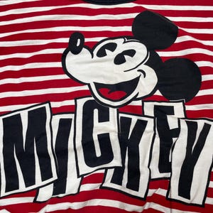 May include: Red and white striped shirt with a black and white Mickey Mouse graphic and the word "Mickey" printed in black letters.