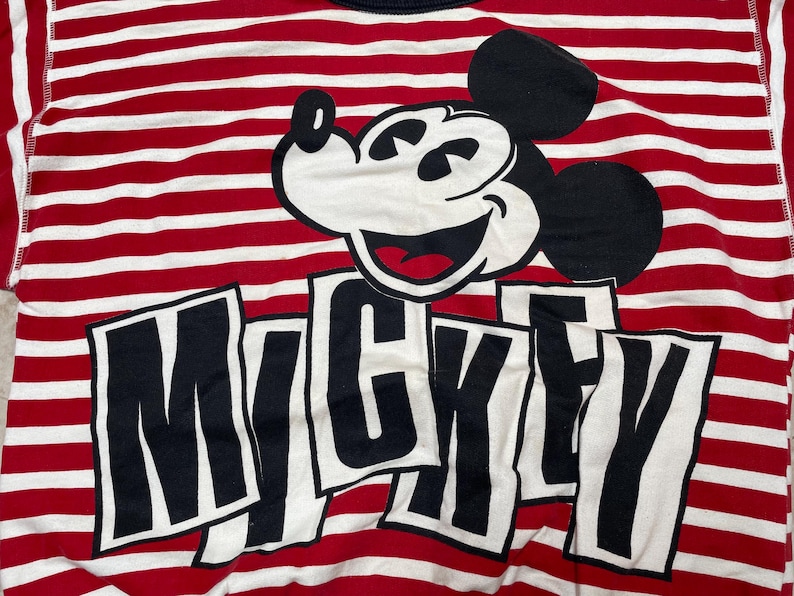 May include: Red and white striped shirt with a black and white Mickey Mouse graphic and the word "Mickey" printed in black letters.