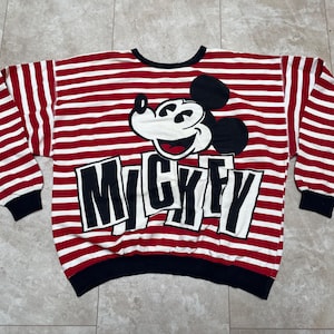 May include: Red and white striped long-sleeve shirt with a black and white Mickey Mouse graphic and the word "Mickey" printed in black letters.
