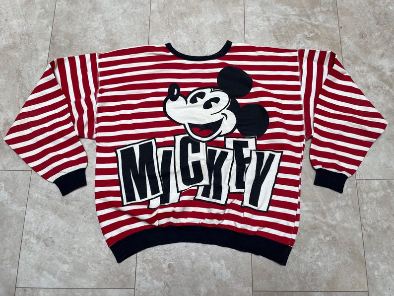 May include: Red and white striped long-sleeve shirt with a black and white Mickey Mouse graphic and the word "Mickey" printed in black letters.
