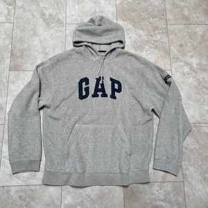 Peut inclure: Un sweat à capuche gris avec un logo "GAP" bleu marine sur le devant. Le sweat-shirt a une poche kangourou et une capuche à cordon.