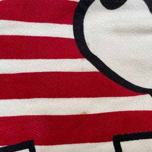 May include: Red and white striped fabric with a black and white cartoon character design. The character is a simple stick figure with a large head and a small body.