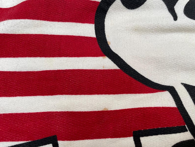 May include: Red and white striped fabric with a black and white cartoon character design. The character is a simple stick figure with a large head and a small body.