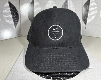 Könnte beinhalten: Eine schwarze Baseballkappe mit einem weißen Nike-Swoosh-Logo und einem weißen Kreis mit einem Golfclub-Design. Der Text "Nike" ist auf die Kappe gestickt.