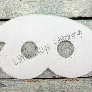 May include: White felt eye mask with two eye holes and a jagged edge on the left side. The mask has the text "Little Guys Stitching" printed on it.