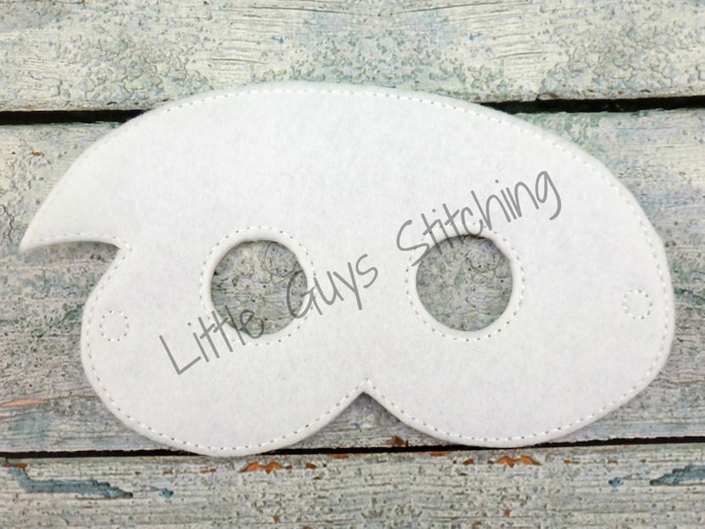May include: White felt eye mask with two eye holes and a jagged edge on the left side. The mask has the text "Little Guys Stitching" printed on it.