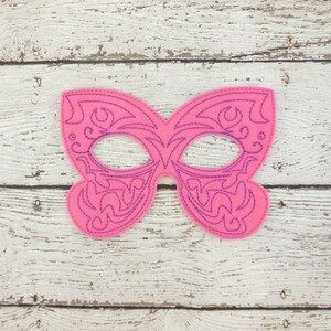 May include: A pink felt masquerade mask with a purple intricate design. The mask has two eye holes and is shaped like a butterfly.