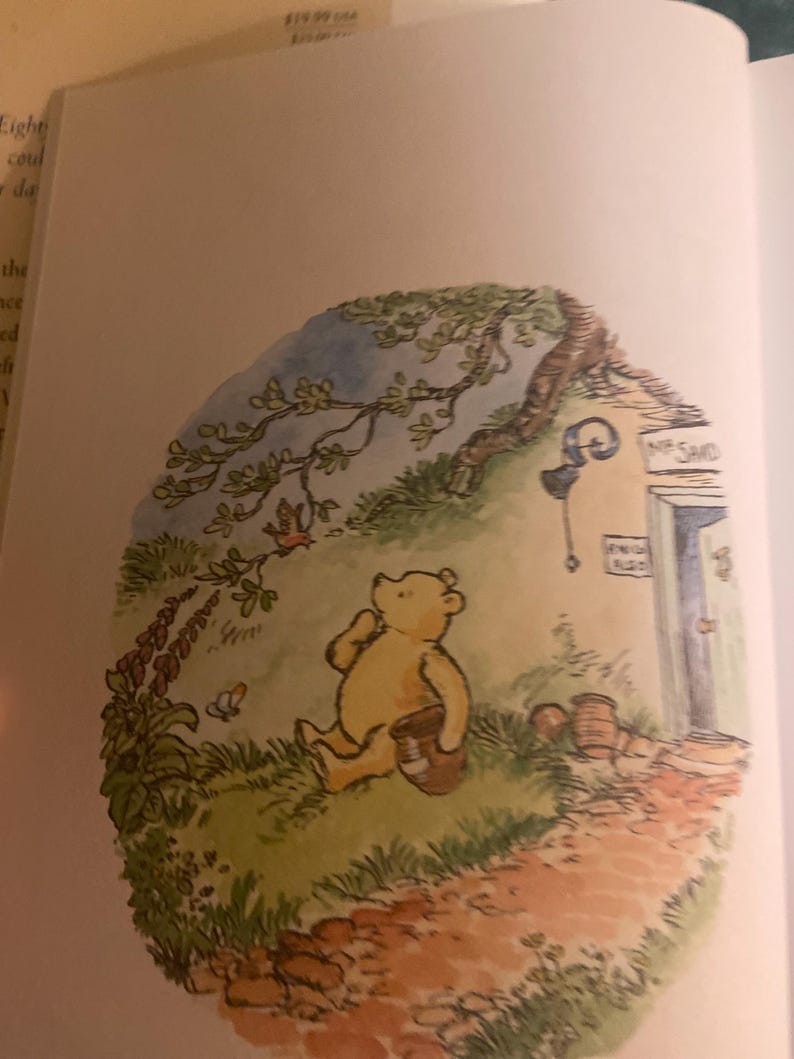 Pode incluir: Uma ilustra&ccedil;&atilde;o em aquarela do Winnie the Pooh sentado em um caminho em uma floresta. Ele est&aacute; segurando uma panela em sua m&atilde;o e olhando para cima para uma &aacute;rvore. A ilustra&ccedil;&atilde;o est&aacute; em uma moldura circular com um fundo azul claro.