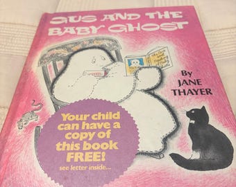 May include: A children's book titled Gus and the Baby Ghost by Jane Thayer with pictures by Seymour Fleishman. The pink cover features a white ghost sitting in a chair reading a book, a black cat, and a mouse. A purple circular sticker reads: Your child can have a copy of this book FREE! see letter inside...