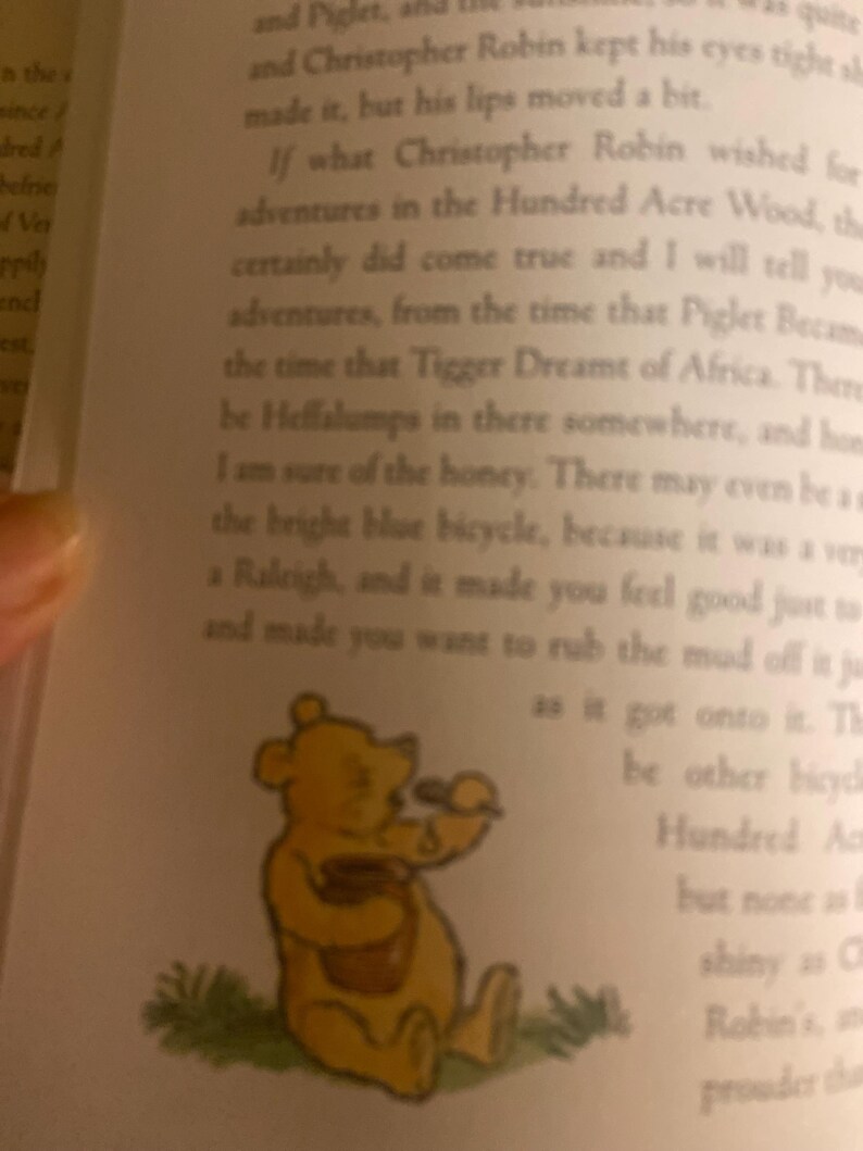 Pode incluir: Um urso de desenho animado amarelo vestindo uma camisa vermelha e segurando um pote de mel. O urso est&aacute; sentado em um peda&ccedil;o de grama verde. O texto na imagem diz: "Se o que Christopher Robin desejava para aventuras na Floresta dos Cem Acres, o certamente se tornou realidade e eu vou te contar aventuras, desde o momento em que Porquinho se tornou o momento em que Tigger sonhou com a &Aacute;frica. H&aacute; Heffalumps por a&iacute; em algum lugar, e mel, tenho certeza. Pode haver at&eacute; um a bicicleta azul brilhante, porque era um muito um Raleigh, e te fazia sentir bem s&oacute; para e te fazia querer esfregar a lama dela justo quando subia nela. H&aacute; outras bicicletas Cem Acres mas nenhuma &eacute; t&atilde;o brilhante quanto a de Christopher Robin e mais orgulhosa do que"