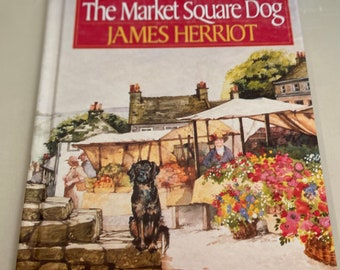 Könnte beinhalten: Ein gebundenes Buch mit dem Titel The Market Square Dog von James Herriot, illustriert von Ruth Brown. Das Cover zeigt eine Aquarellillustration eines schwarzen Hundes, der auf einer Steinmauer vor einem Markt mit bunten Blumen sitzt.