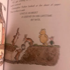 Pode incluir: Uma ilustra&ccedil;&atilde;o de um livro infantil que mostra um grupo de coelhos e um urso. Os coelhos est&atilde;o cavando um buraco no ch&atilde;o, enquanto o urso fica em uma sali&ecirc;ncia acima deles. O texto na p&aacute;gina diz "Tio Robert Uma lenda em sua vida por Wool."