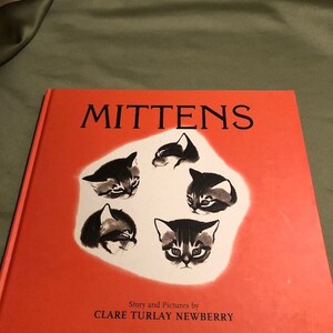 May include: A hardcover book titled MITTENS with a bright orange cover. The center features a white circular area containing five black and white ink illustrations of kitten faces. The text Story and Pictures by CLARE TURLAY NEWBERRY is printed below.