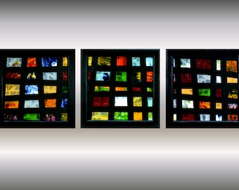 Op de afbeelding: Drie ingelijste vierkante kunstwerken met een zwarte lijst. Elk kunstwerk is een raster van kleurrijke vierkanten in verschillende tinten rood, blauw, groen, geel en oranje.
