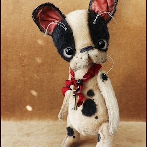 May include: A handmade plush toy dog with black and white fur, wearing a red ribbon with a key attached. The dog has black spots and large, black eyes.