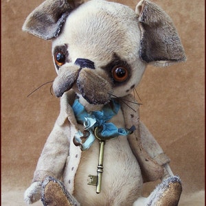 May include: A handmade plush pug dog with a vintage aesthetic. The dog has a cream-colored body, brown accents, and a blue ribbon with a key. The dog is wearing a light brown coat. The text "Alla Bears" is in the top right corner.