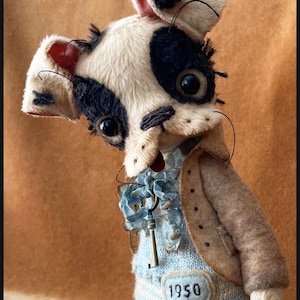 May include: A handmade plush toy dog with black and white fur, wearing a light blue sweater with the number "1950" and a brown jacket. The dog has large, expressive eyes and a key pendant.