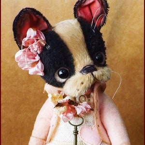 May include: A handmade plush toy dog with black and white fur, wearing a pink jacket and a white dress with a pink heart. The dog has a pink flower on its head and a key around its neck.