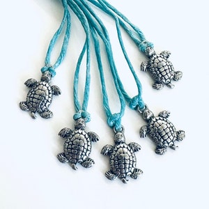 May include: Five teal blue cords with silver turtle charms attached. The turtles are detailed with textured shells and have a slightly raised head.