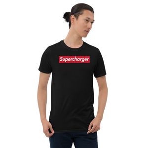 Puede incluir: Camiseta negra con la palabra "Supercharger" en texto blanco dentro de un rectángulo rojo. La camiseta es de manga corta. La persona de la imagen lleva la camiseta.