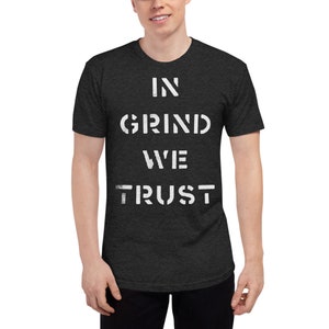 May include: Dark gray t-shirt with the white text "IN GRIND WE TRUST" in a stencil font. The shirt is short-sleeved and has a crew neck.