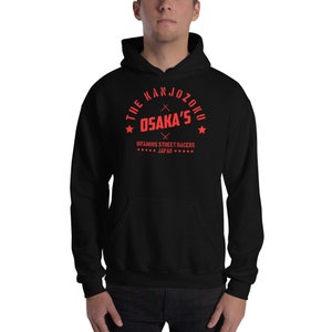 May include: Black hooded sweatshirt with a red graphic. The graphic reads "THE KANJOZOKU OSAKA'S INFAMOUS STREET RACERS JAPAN" in a circular design with stars and crossed lines. The sweatshirt has a front pocket and a drawstring hood.