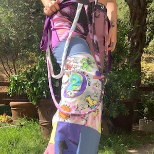 May include: Purple, pink, blue, and white patchwork pants with a tie at the waist. The pants have a Grateful Dead logo and tie-dye pattern.