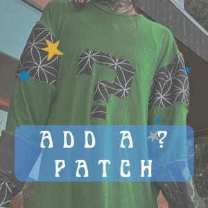 Pode incluir: Camiseta verde de manga comprida com padrões geométricos preto e branco nas mangas. Um grande ponto de interrogação preto com um padrão geométrico branco está na frente da camiseta. O texto "ADD A PATCH?" está em uma faixa azul.