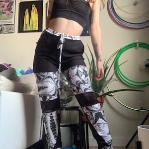 Può includere: Pantaloni della tuta a fantasia bianca e nera con vita con coulisse. I pantaloni presentano un design unico con pannelli a contrasto di motivi a paisley bianchi e neri. La modella indossa un top a fascia nero e scarpe da ginnastica bianche.