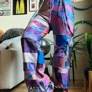 Può includere: Pantaloni patchwork viola, blu e rosa con un laccio in vita. I pantaloni presentano una varietà di motivi astratti e geometrici.