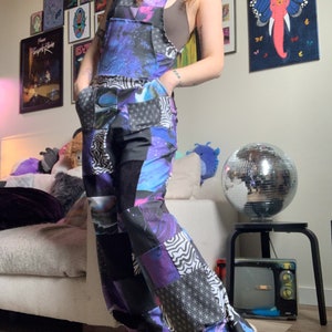 May include: A pair of blue and black patchwork overalls with a galaxy print. The overalls have a wide leg and are made of a soft, comfortable fabric.