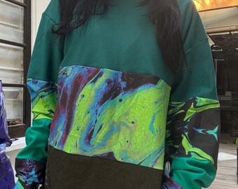 May include: A long-sleeved shirt with a green, blue, and black abstract print. The shirt has a high neck and a relaxed fit.
