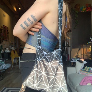 Pode incluir: Uma bolsa tote preta e branca com um padrão geométrico. A bolsa tem uma alça longa e é feita de um tecido macio e felpudo.