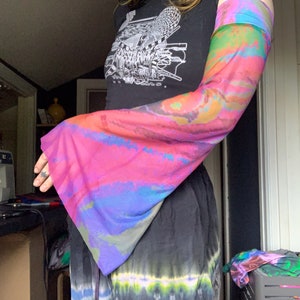 Pode incluir: Um top preto curto com uma estampa gráfica de um pássaro e formas geométricas. O top tem uma manga tie-dye com cores rosa, azul e verde.