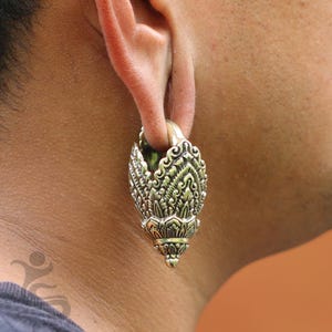 May include: Ornate brass-colored ear gauge with detailed floral and scrollwork design. The gauge is worn in a stretched earlobe, showcasing the intricate patterns and textures of the jewelry. The gauge has a flared, rounded shape.