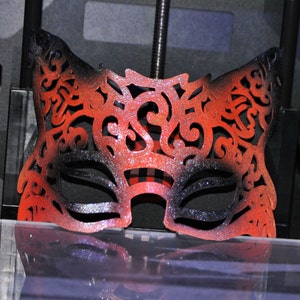 May include: A red and black masquerade mask with intricate cutouts and glitter. The mask is made of a lightweight material and has a delicate, feminine design.