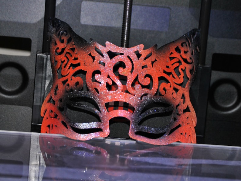 May include: A red and black masquerade mask with intricate cutouts and glitter. The mask is made of a lightweight material and has a delicate, feminine design.