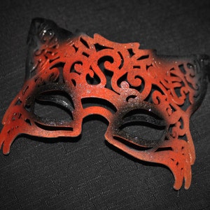 May include: A black and orange masquerade mask with intricate cutouts and glitter accents.