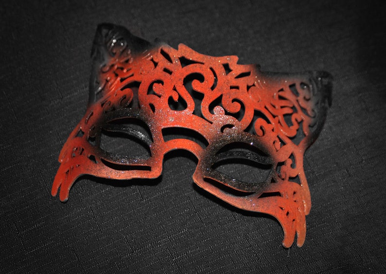 May include: A black and orange masquerade mask with intricate cutouts and glitter accents.