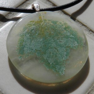 May include: A round glass pendant necklace with a green and yellow marbled design. The pendant is on a black cord.