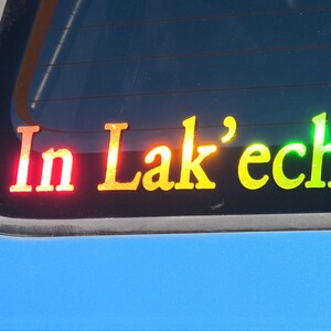 May include: A rear window sticker with the words "In Lak'ech" in rainbow colors. The sticker is on a blue car.